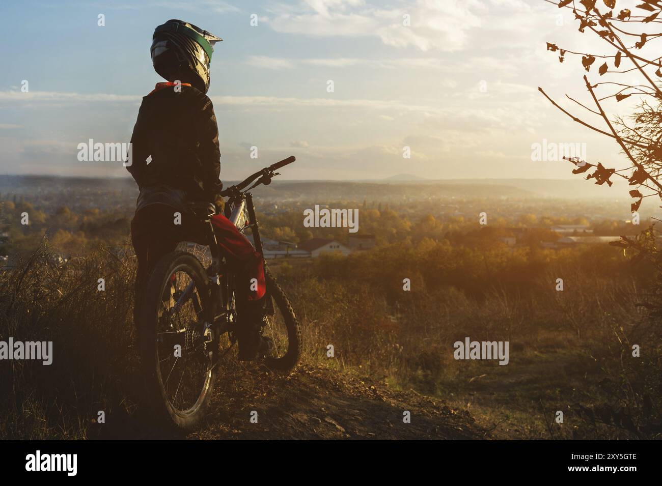 Portrait of a young rider in full protection of a full face helmet mask and gloves on a bicycle on sunset landscape. The concept of involving young pe Stock Photo