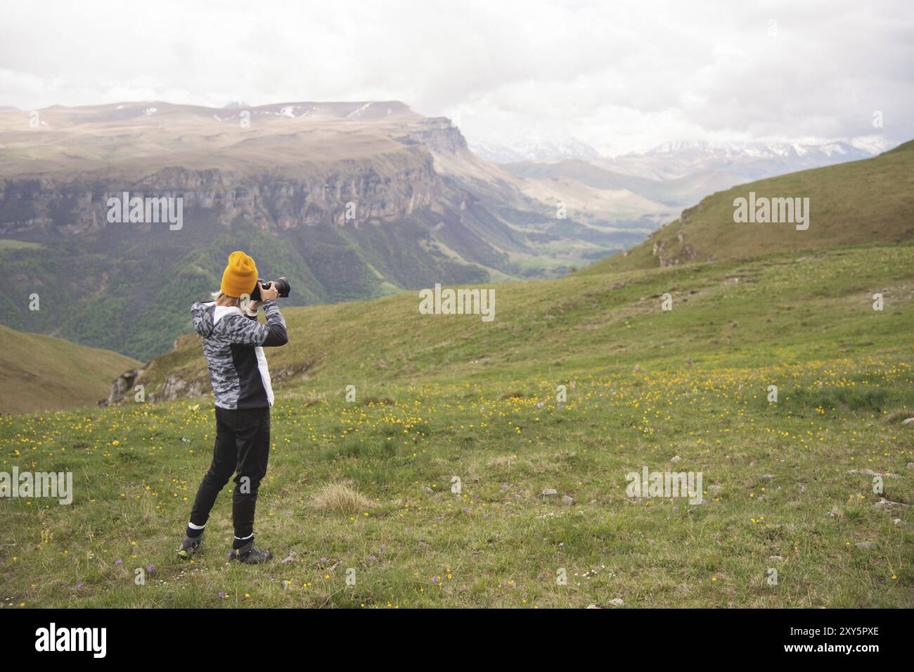 A young girl takes pictures of a plateau on top of a high mountain on a cloudy day. View of the girl behind Stock Photo