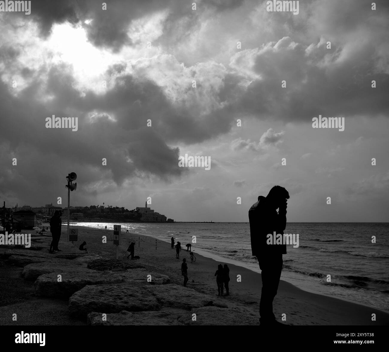 Evening on sea shore with silhouettes and moon behind clouds Stock Photo