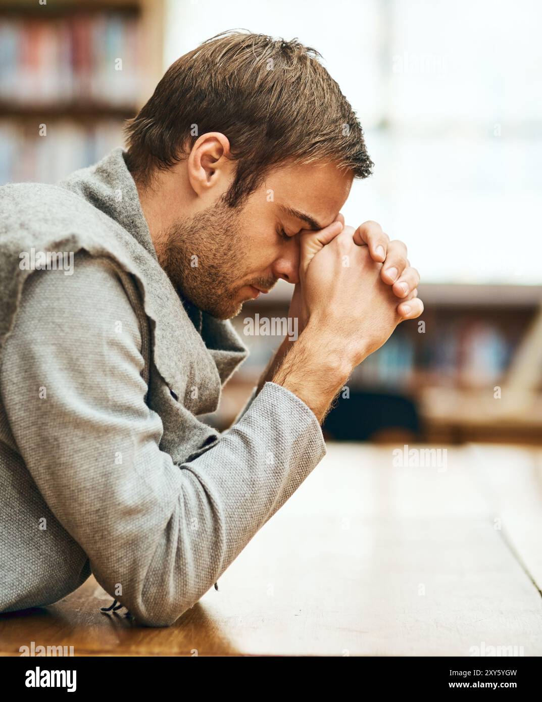 Student, praying and spiritual in university for study, worship and college scholarship in library. Man, faith and meditation to God on campus for Stock Photo