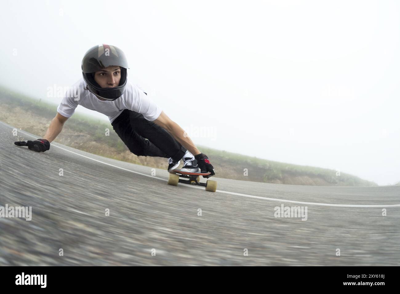 A young guy in a full face helmet on a country road in a slide passes a turn against a background of low clouds and fog Stock Photo