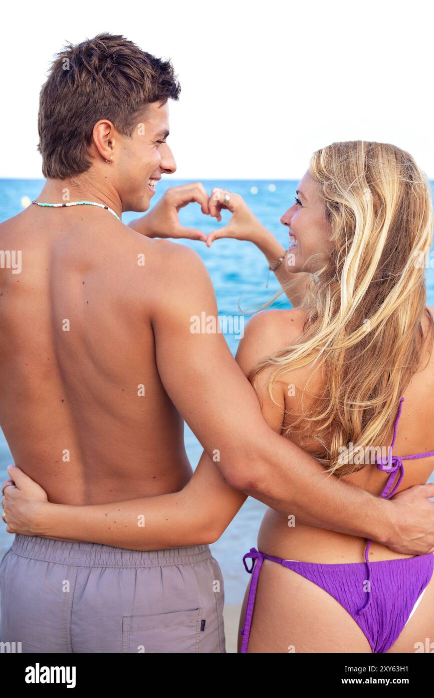 Young couple making heart shape with their hands on the beach looking at camera Stock Photo
