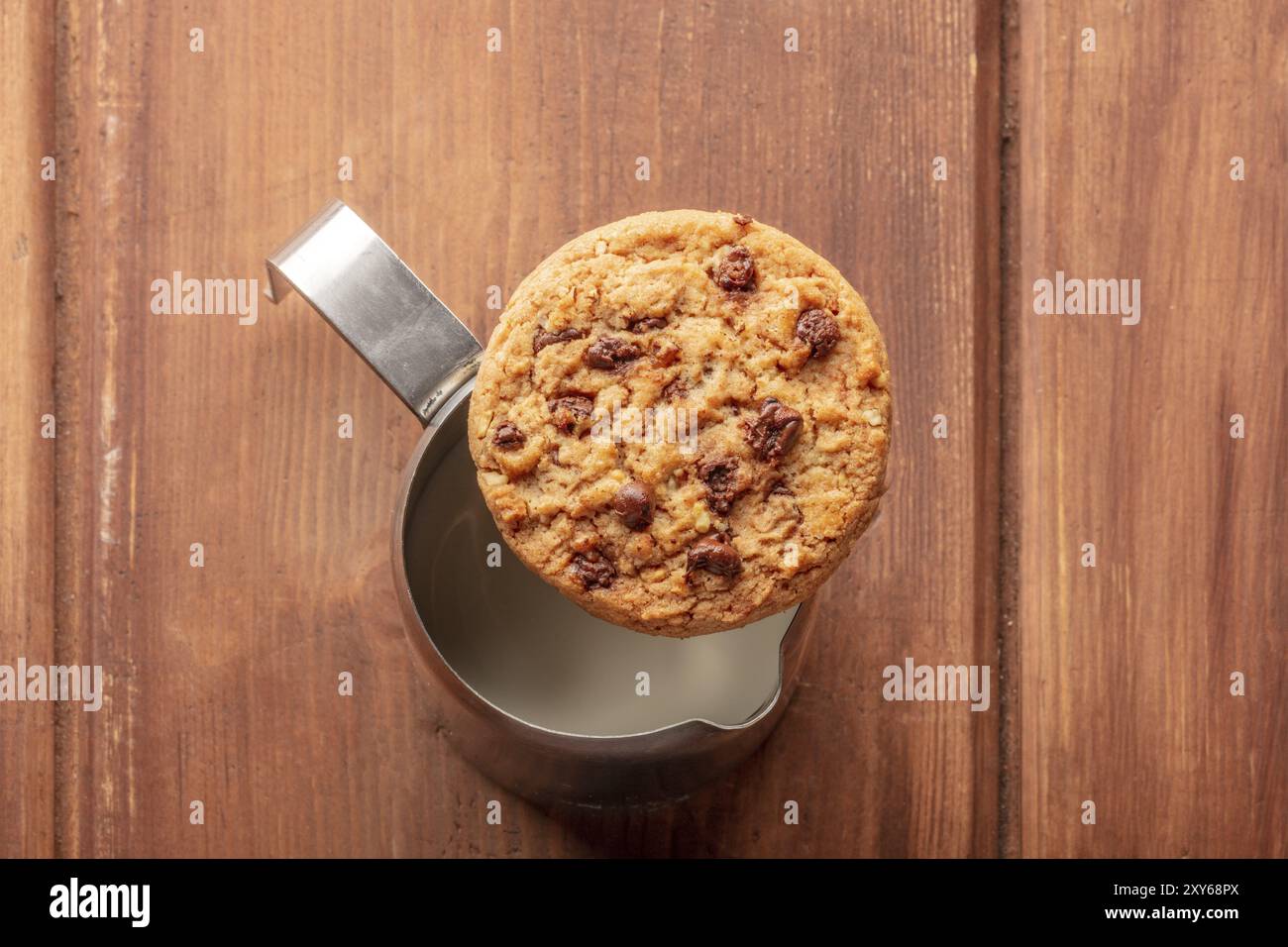 Good morning. A chocolate chip cookie, shot from above on top of a milk jug, on a dark rustic wooden table with a place for text Stock Photo