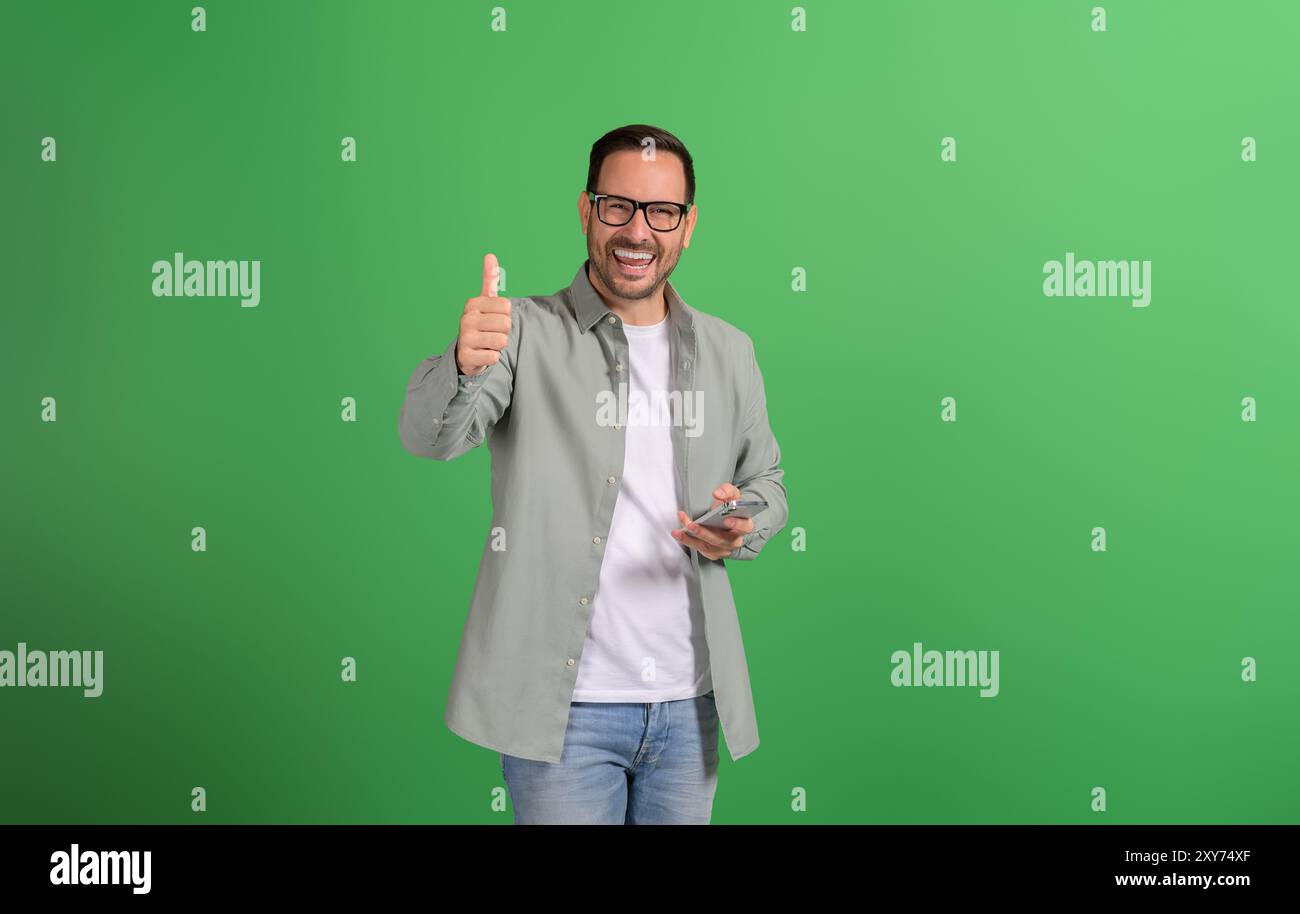 Portrait of ecstatic male influencer showing thumbs sign and using ...