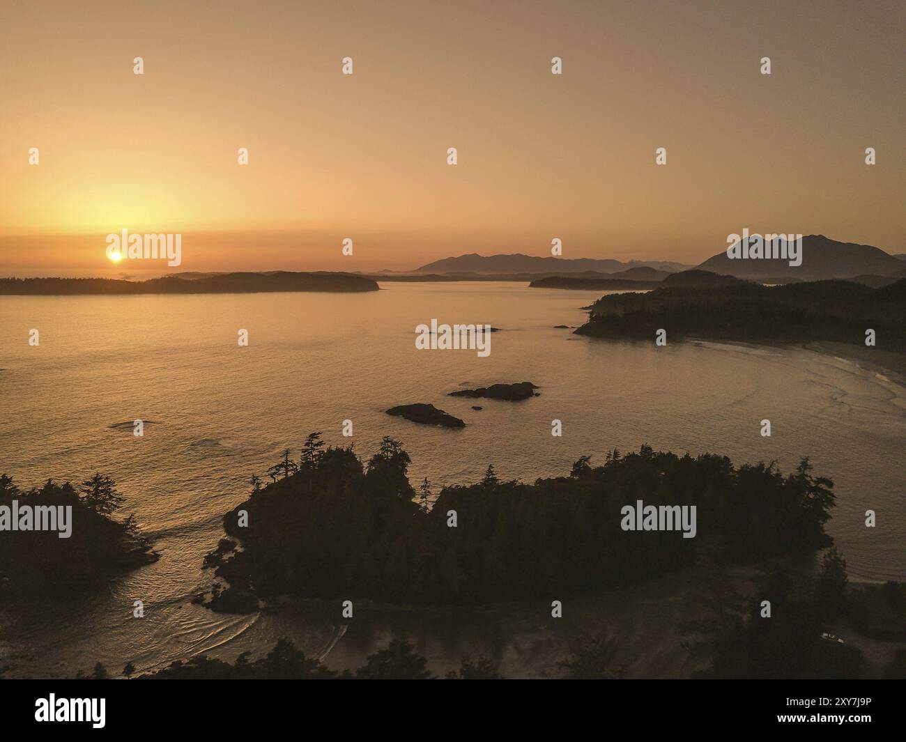 Serene sunset over a calm ocean with silhouetted islands and trees, creating a peaceful and tranquil atmosphere, Tofino, BC, Canada, North America Stock Photo