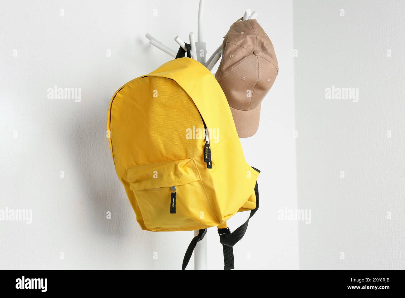 Yellow backpack and cap hanging on white wall Stock Photo