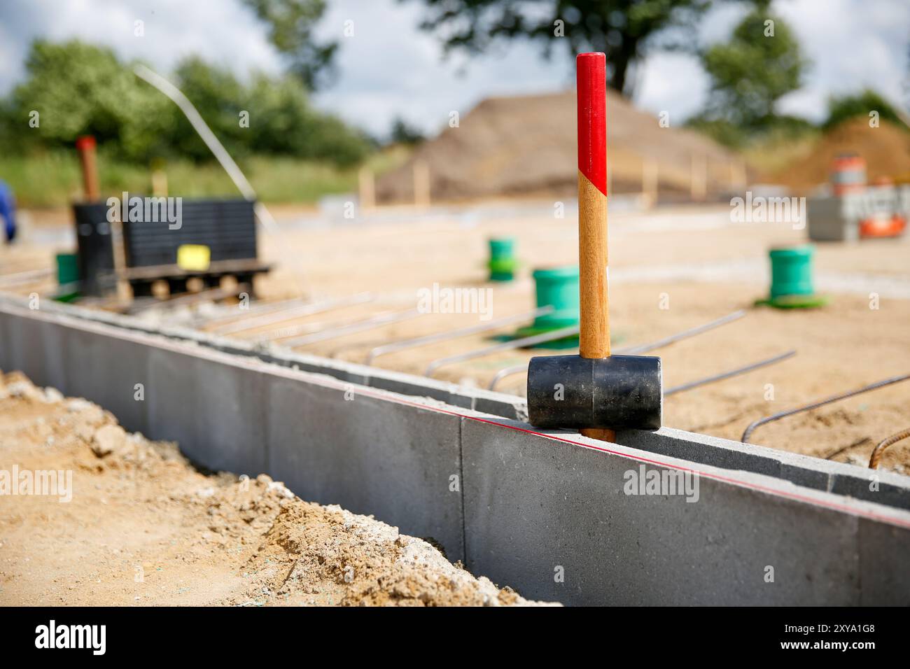 Close up of a rubber hammer standing on concrete curb stones, blurry background wit construction site workers  Stock Photo