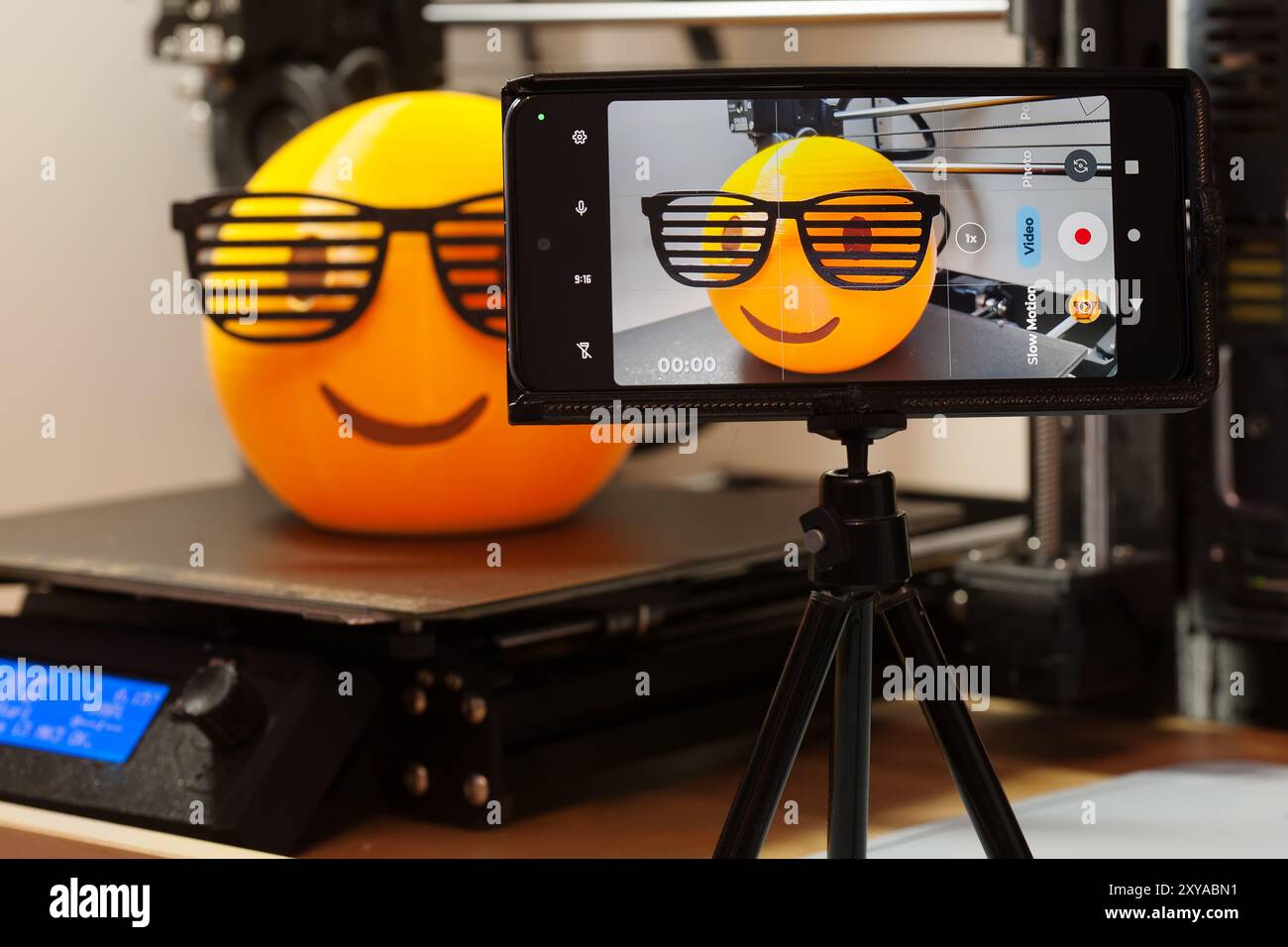 Phone camera monitoring a successful multi-colored 3d print of an emoji with 80's shutter shades on a 3d printer bed, with support material removed Stock Photo