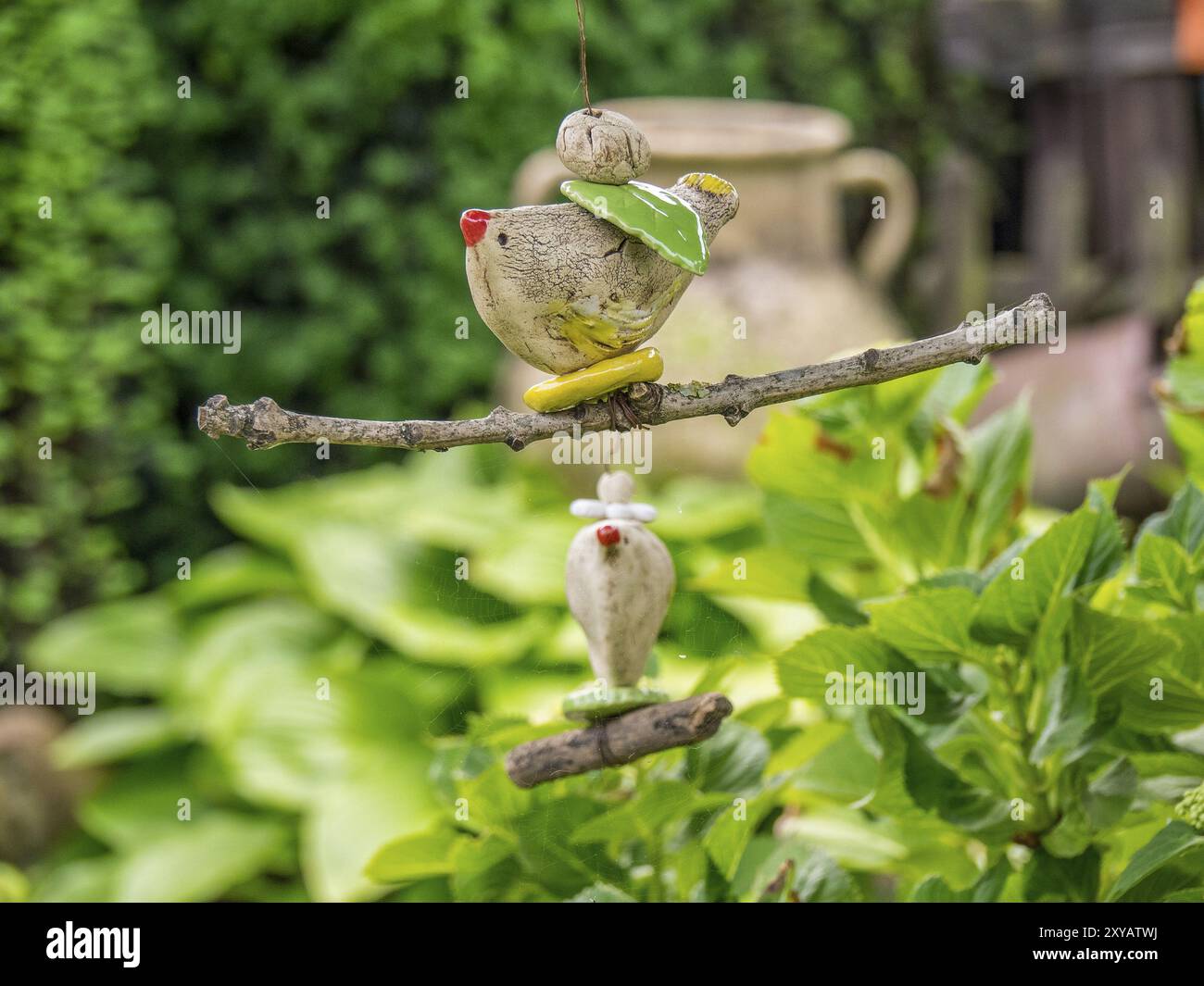 Filigree garden pendant in the shape of a bird on a branch, surrounded by green leaves and a rustic clay jug in the background, borken, muensterland, Stock Photo