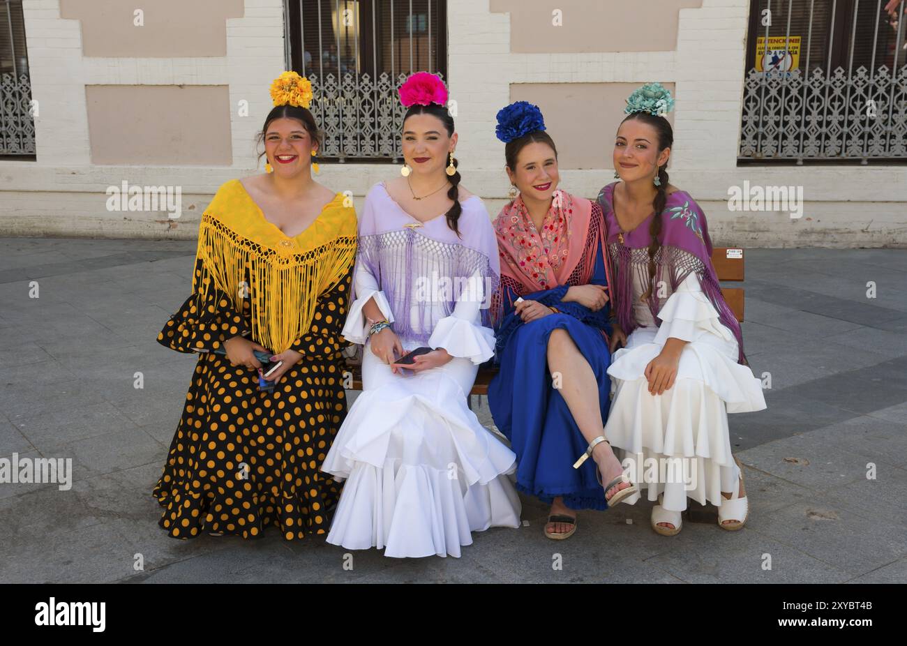 Four woman in colourful flamenco dresses and flowers in their hair sit on a  bench on a street in traditional Spanish fashion, Feria de la Manzanilla  Stock Photo - Alamy