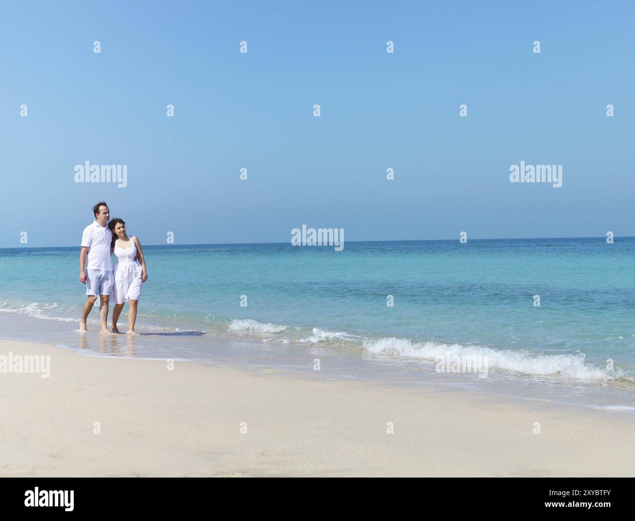 Young happy couple walking on the beach smiling holding around each ...