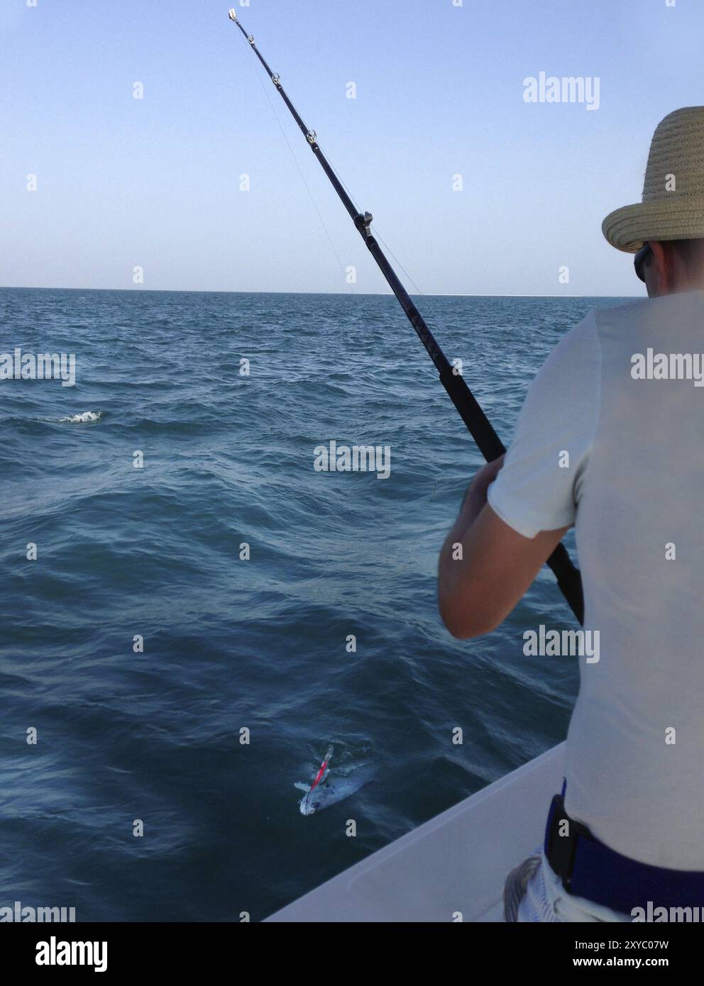 Young man fishing on a ocean. Catching big Queen fish Stock Photo