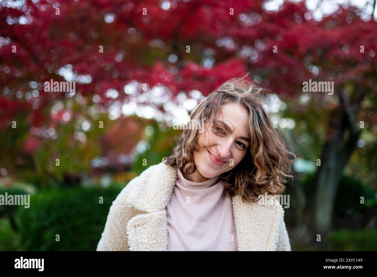 A young woman with curly hair smiles warmly while enjoying a crisp ...