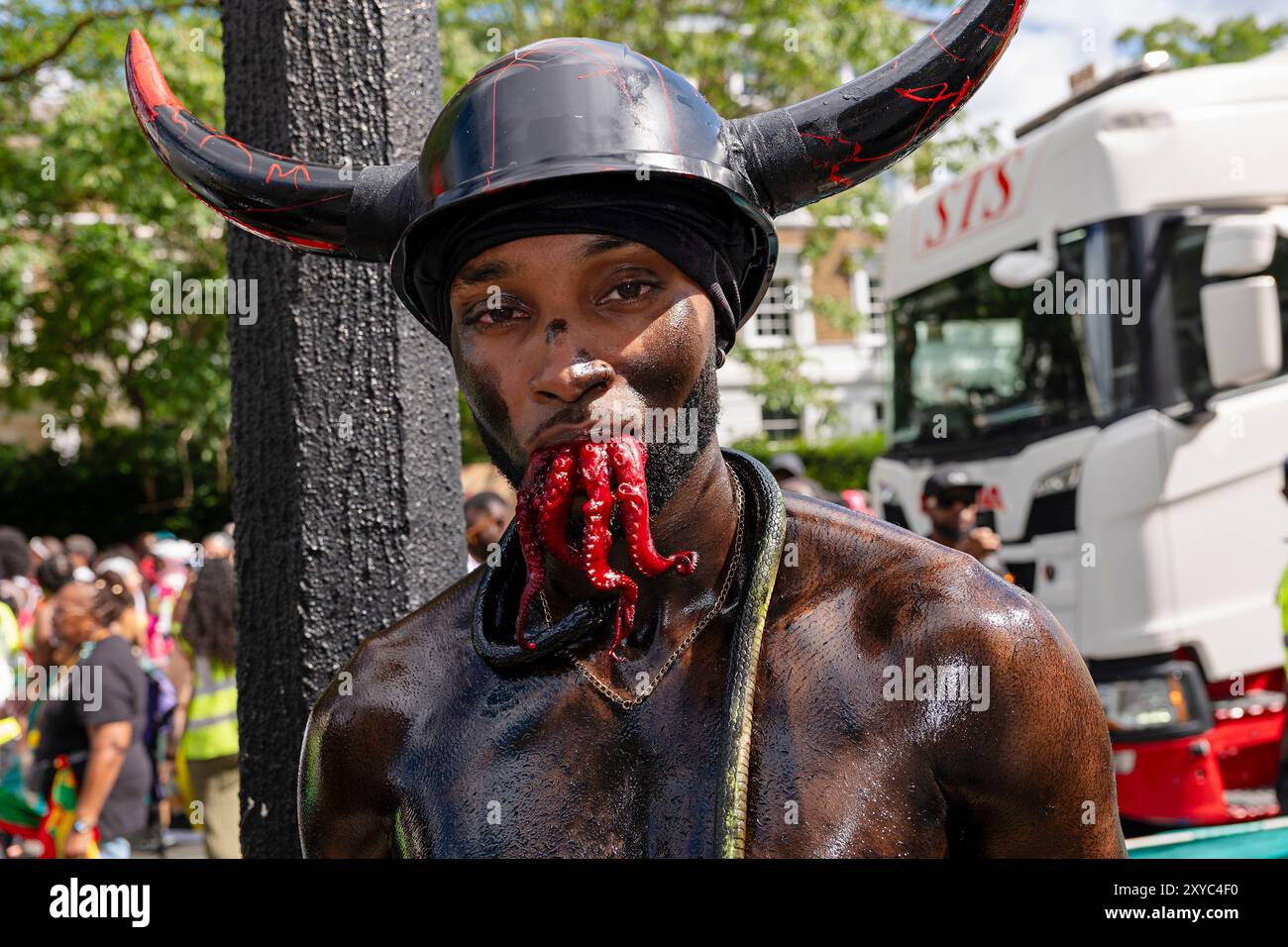 Jab Jab dates back to the Plantations of Grenada during the days of slavery.  The oil, grease and black paint are substitute for the molasses that was used to cover their body. Thick heavy chains are dragged in the streets, goat horns worn on heads with red tongues or raw flesh sticking outside their mouths. Other props used include baby strollers with dolls  Oil drums, biscuit tins and conch shells are their instruments as they are beaten hypnotically as the Jab Jab parade through the streets.  Sipping rum, the produce of molasses and their blood and tears Stock Photo