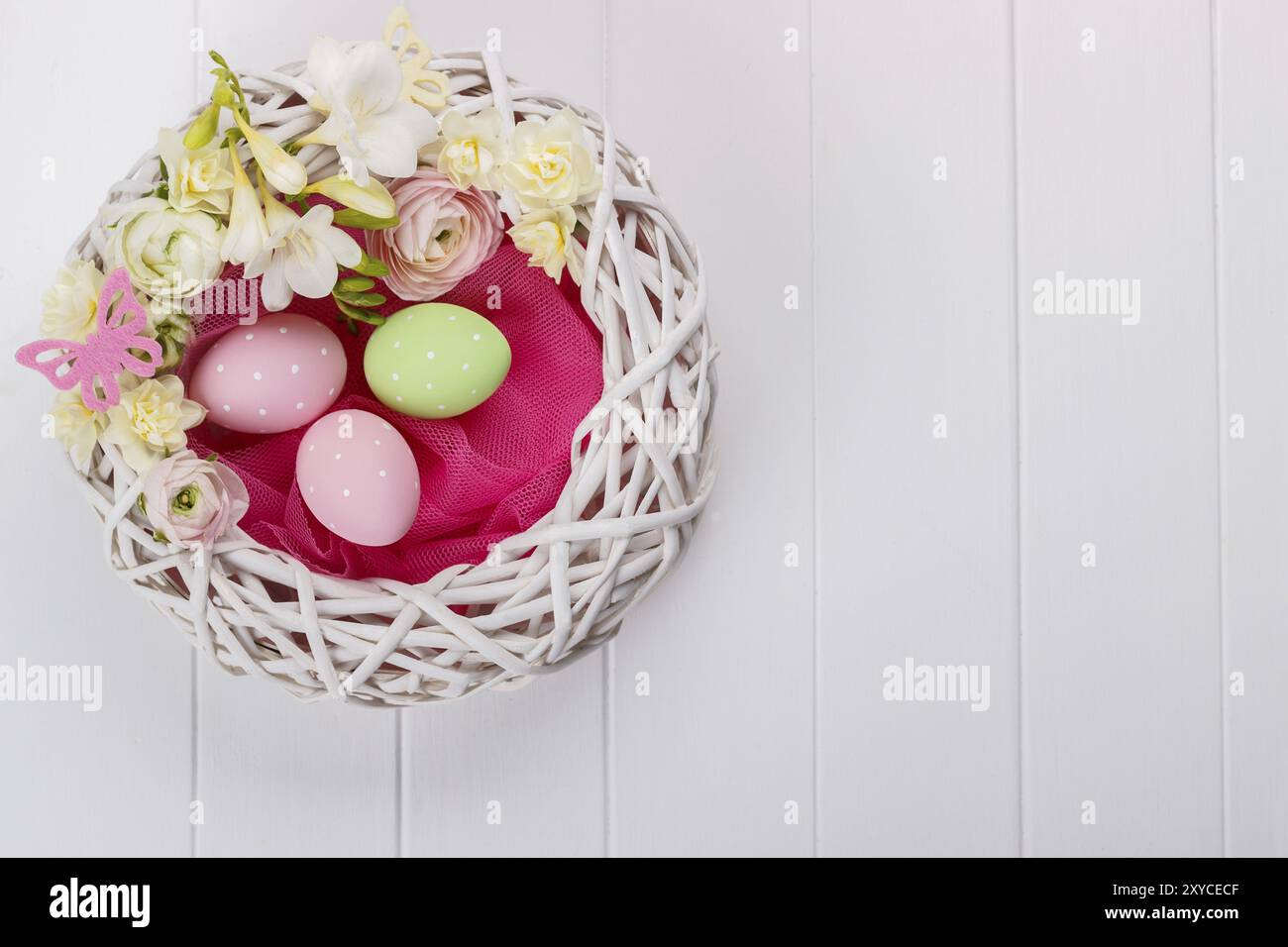 Basket of easter eggs with flowers on white wooden background Stock Photo