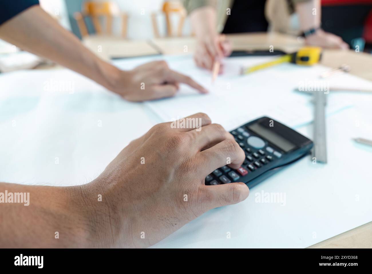 Engineer Working on Blueprint with Calculator and Tools in Office Setting Stock Photo