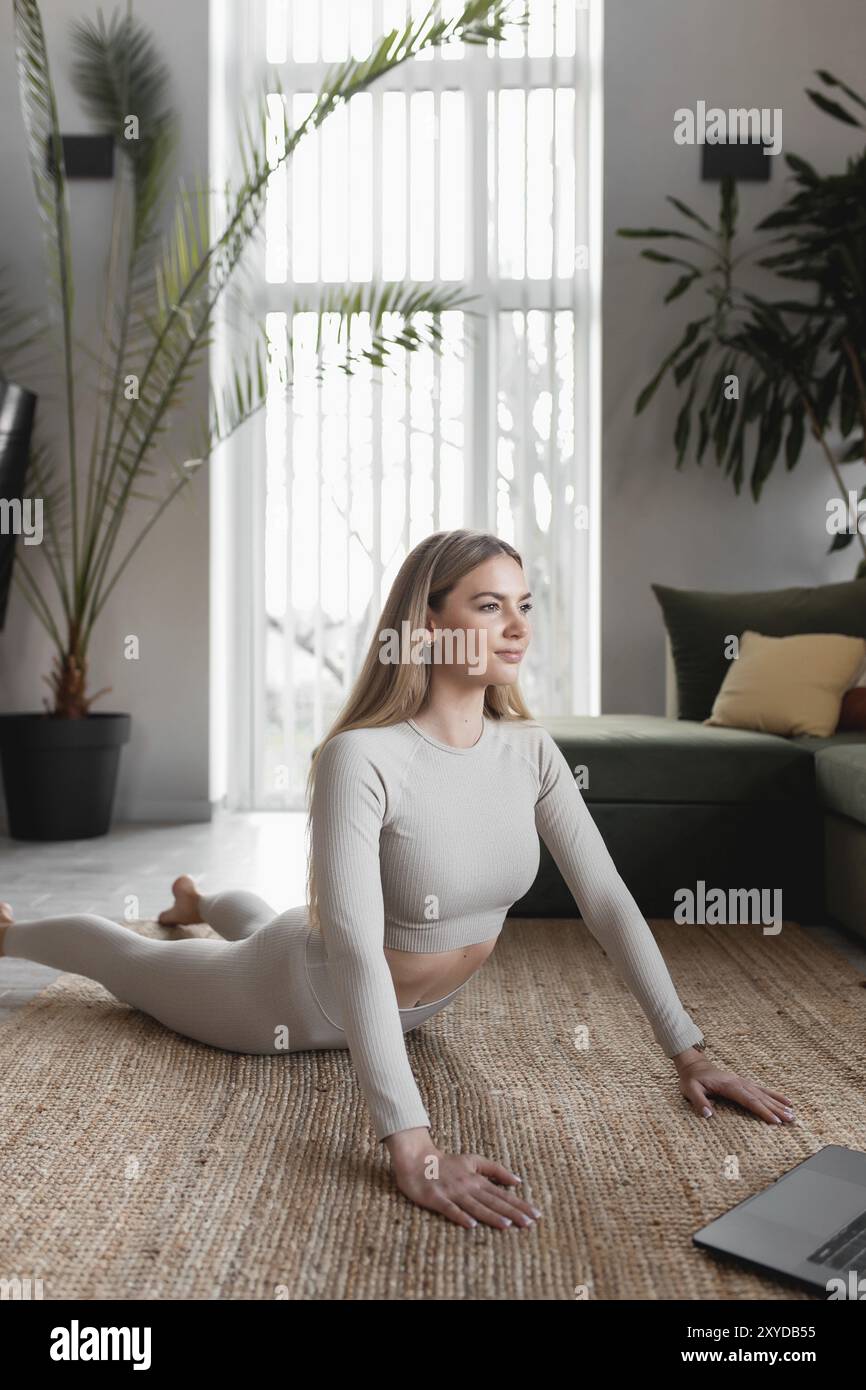 Healthy sport lifestyle concept, happy smiling blogger girl doing yoga exercises at home with green loft interior watching and repeating trainer exerc Stock Photo