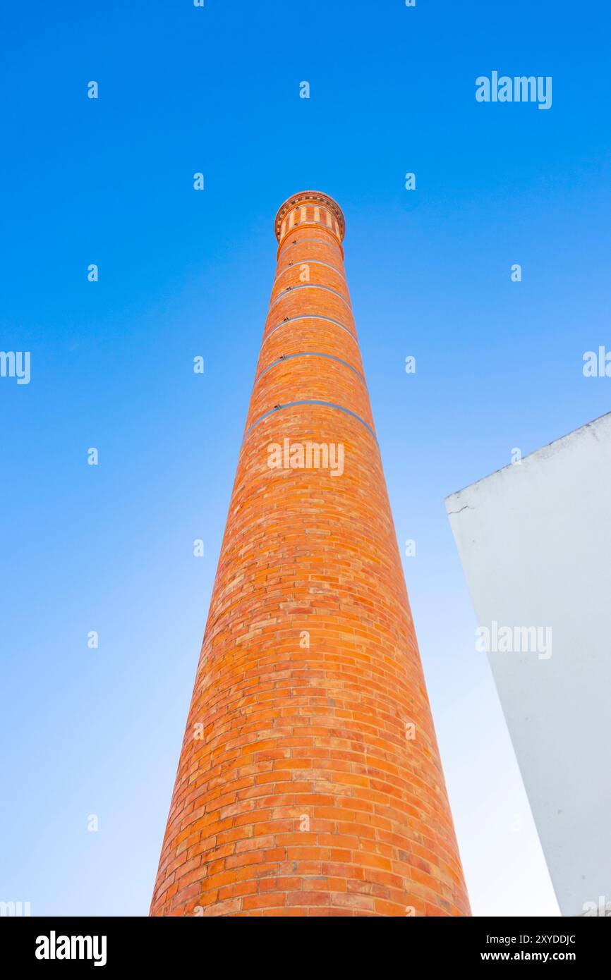 looking up at Tall red brick chimney stack against a clear blue sky with a partial white building on the right side. albufeira portugal Stock Photo