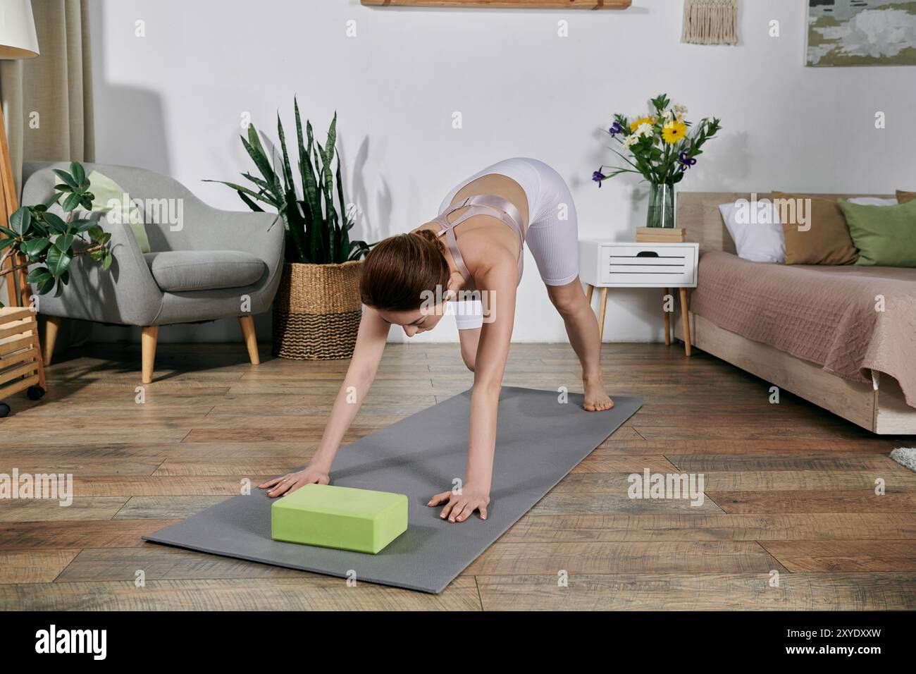 A woman is performing yoga poses on a mat in her living room, using a ...