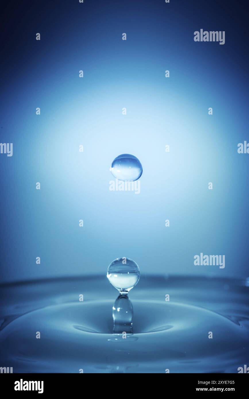 Water drop splashing into a surface blue background Stock Photo - Alamy