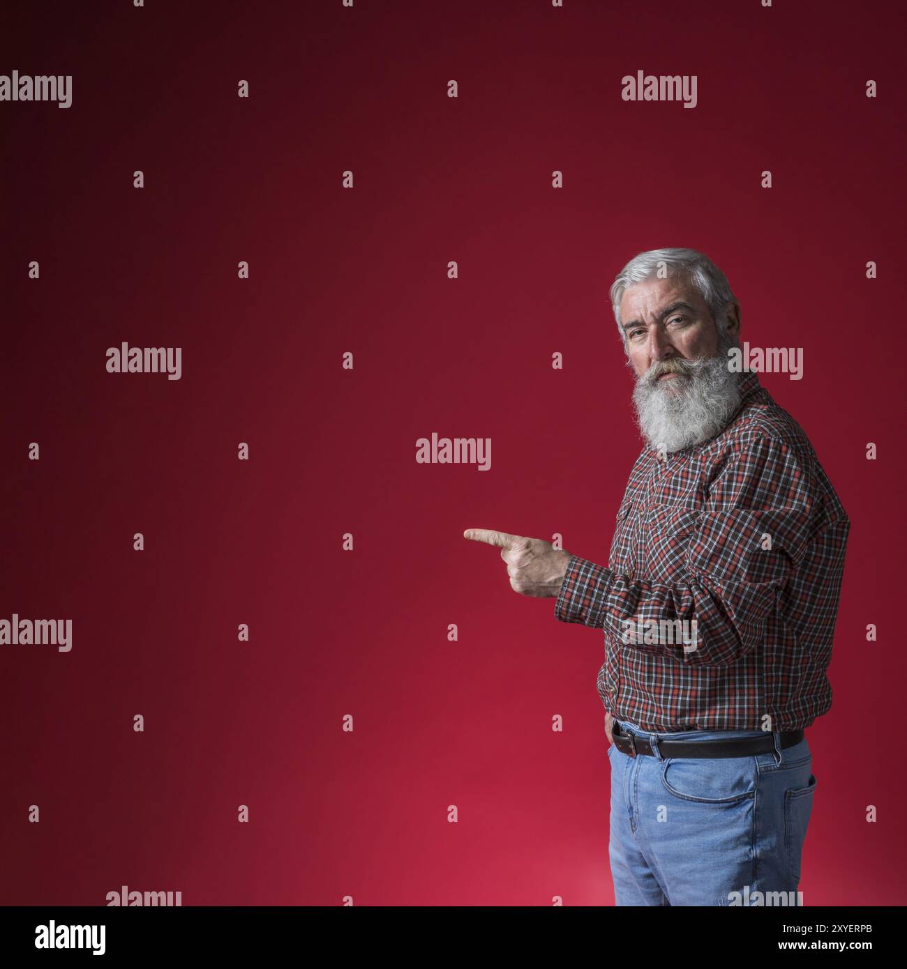 Senior man pointing his finger something against red background Stock Photo