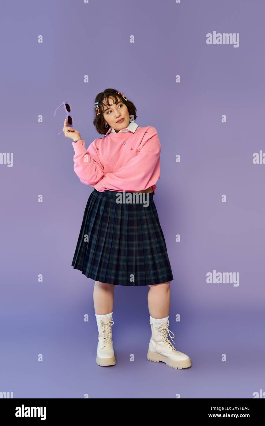 A young woman in a pink sweater and plaid skirt stands in front of a lavender background Stock Photo Alamy