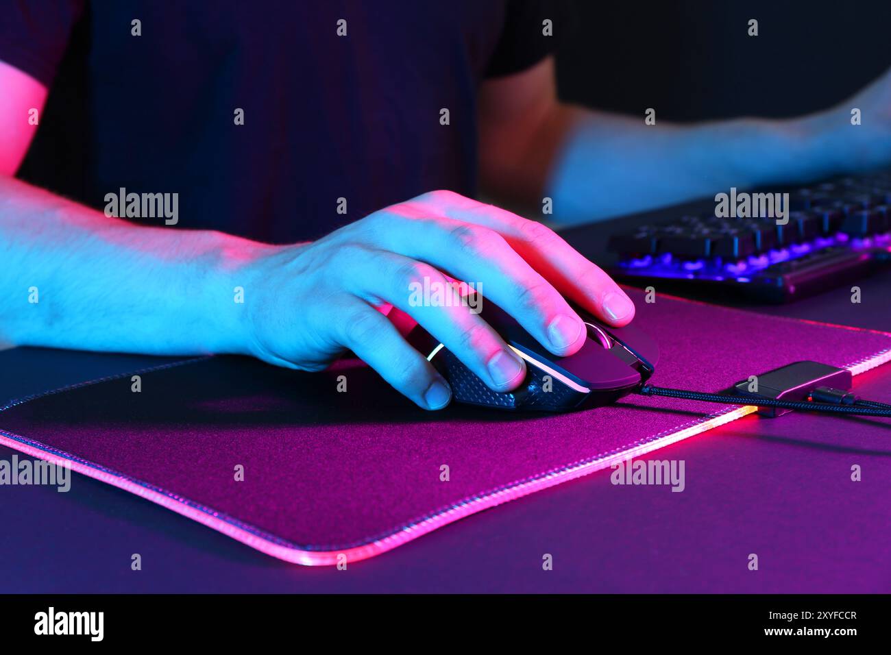 Gamer using modern wired computer mouse in neon lights at dark table ...