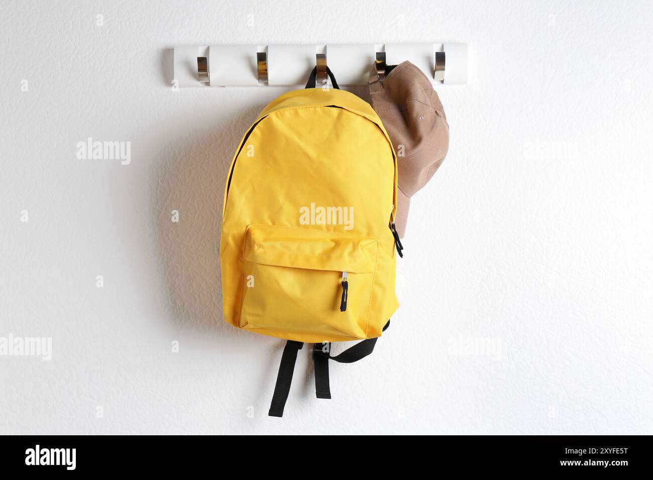 Yellow backpack and cap hanging on white wall Stock Photo