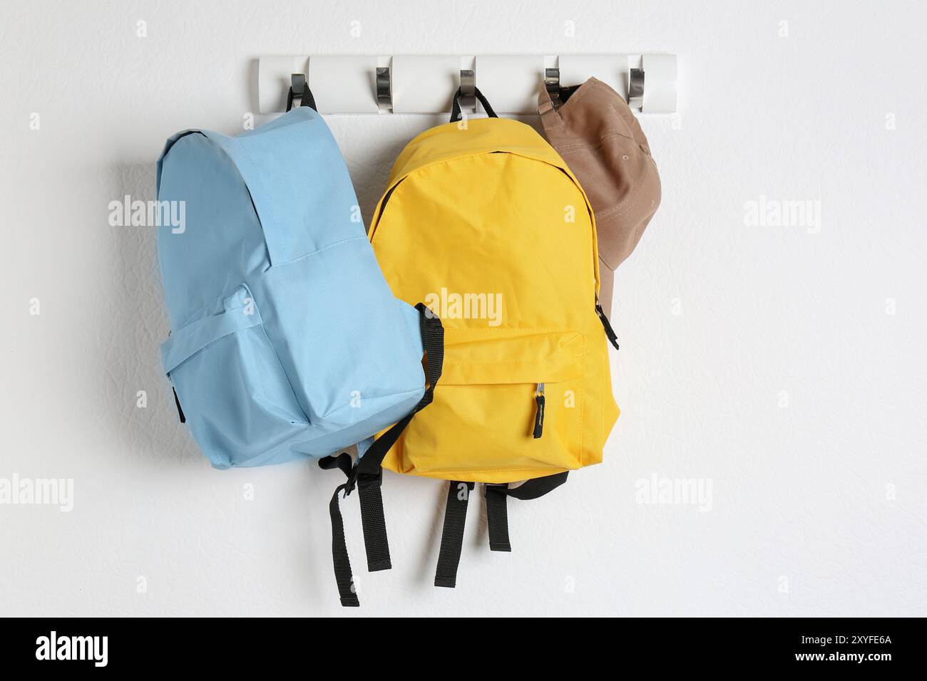 Bright backpacks and cap hanging on white wall Stock Photo