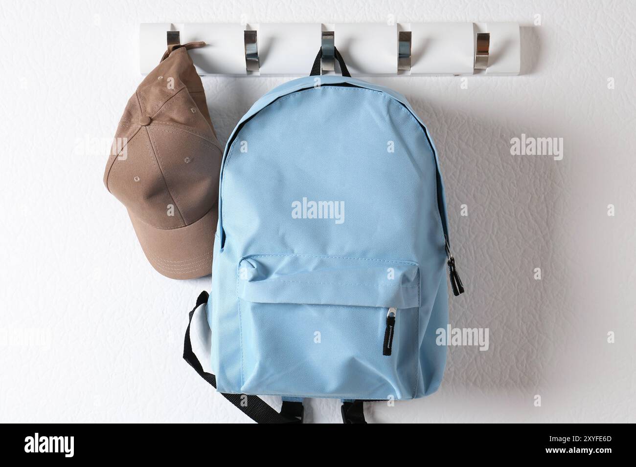Light blue backpack and cap hanging on white wall Stock Photo