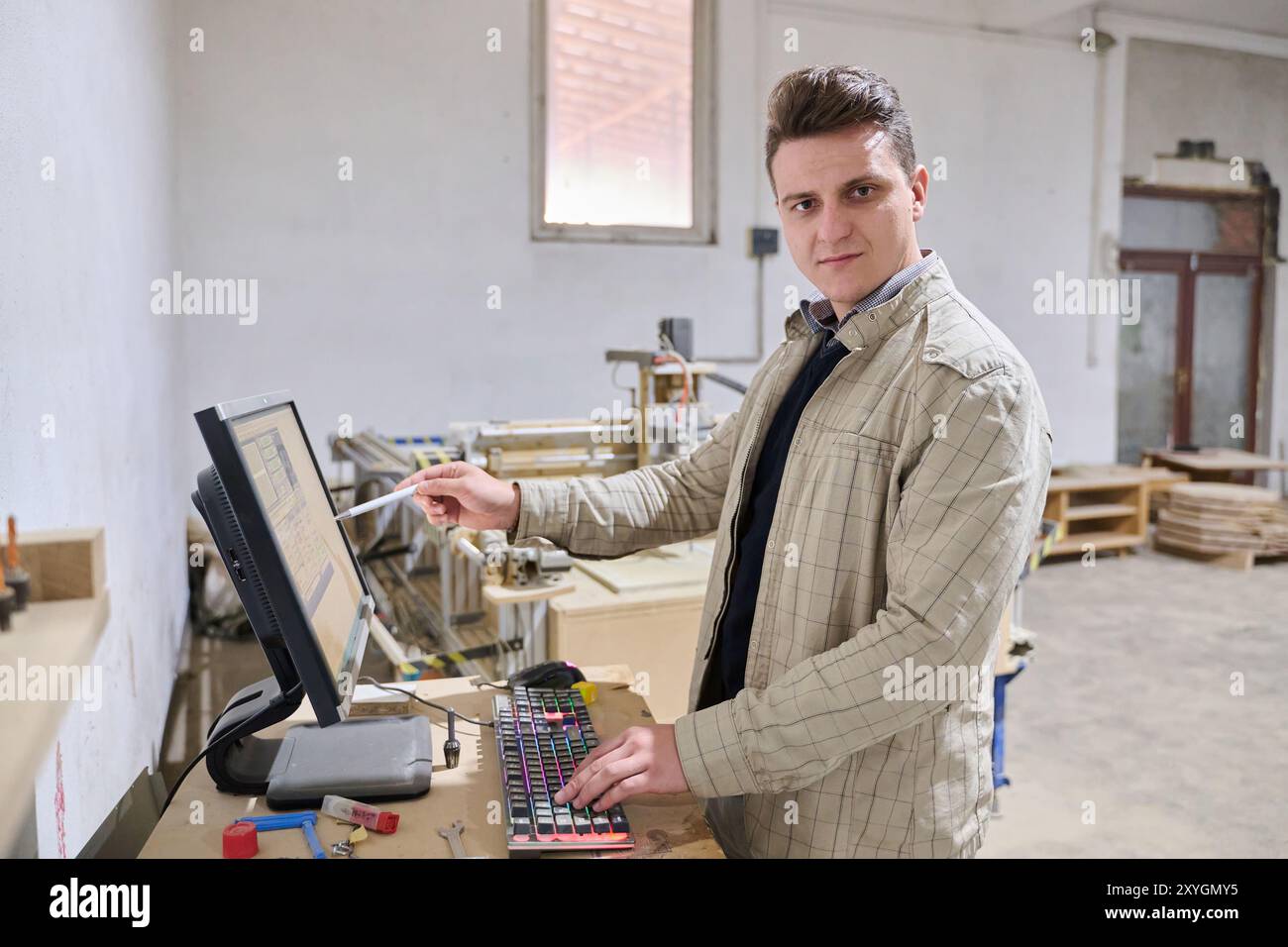 Operator Entering Coordinates on Computer for CNC Machine to Precisely Cut Wooden Pieces Stock Photo