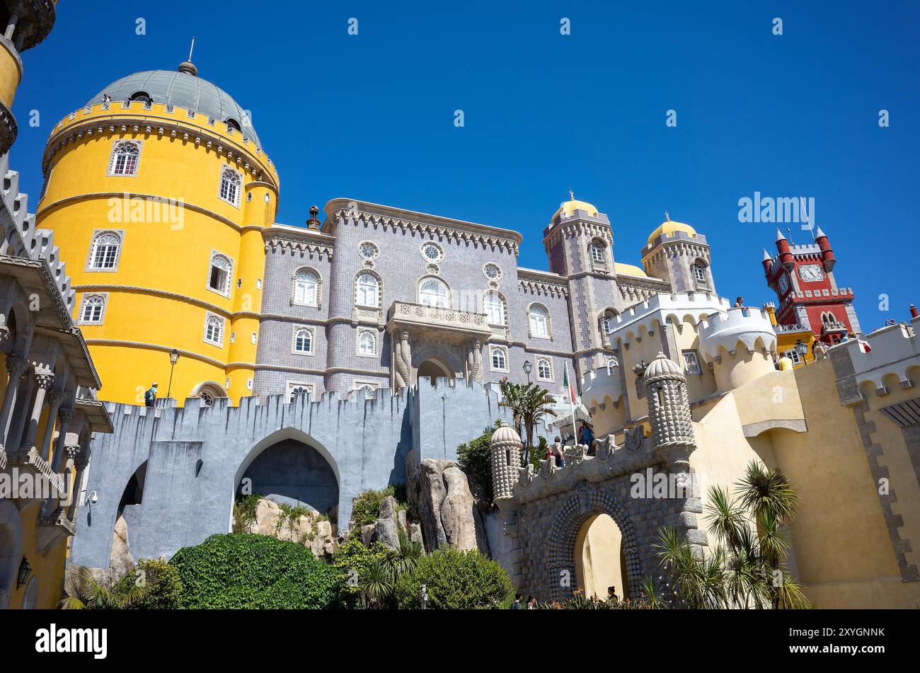 Pena Palace Exterior Architecture Sintra Portugal // SINTRA, Portugal — The vibrant and eclectic exterior architecture of Pena Palace, showcasing its blend of Romanticist, Moorish, and Neo-Manueline styles. The palace's colorful facades, ornate details, and whimsical elements epitomize 19th-century Romantic architecture and King Ferdinand II's vision of a fairytale castle. Stock Photo