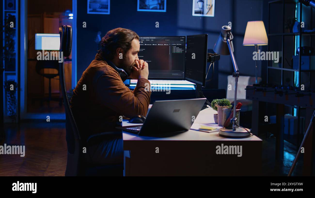 Technician focused on typing complex code in neon lit home office, developing software application. It specialist removing headphones to better concentrate on difficult task, camera B Stock Photo