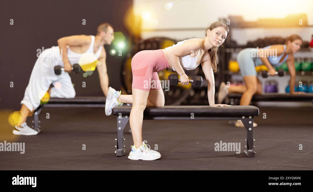 Athletic young woman pumping her biceps with a dumbbell while leaning ...