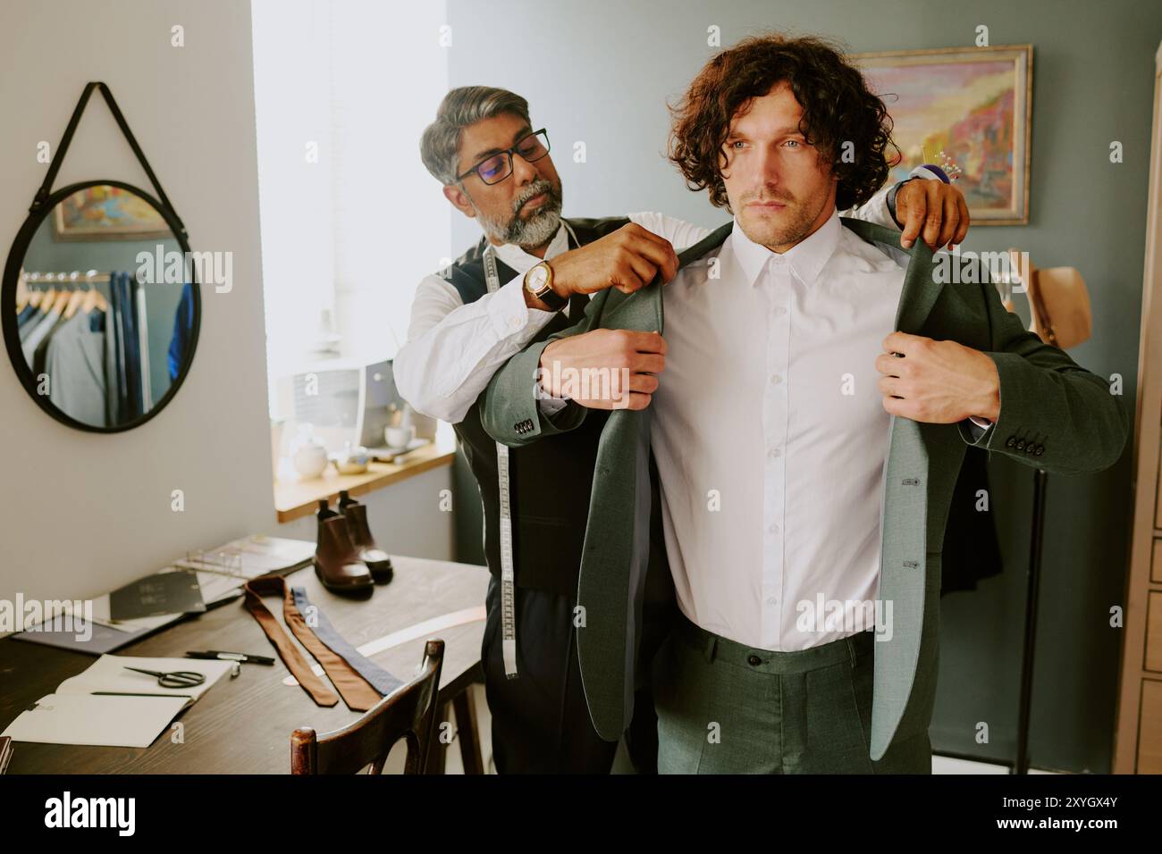 Brutal curly haired model trying on new suit while tailor assisting him Stock Photo