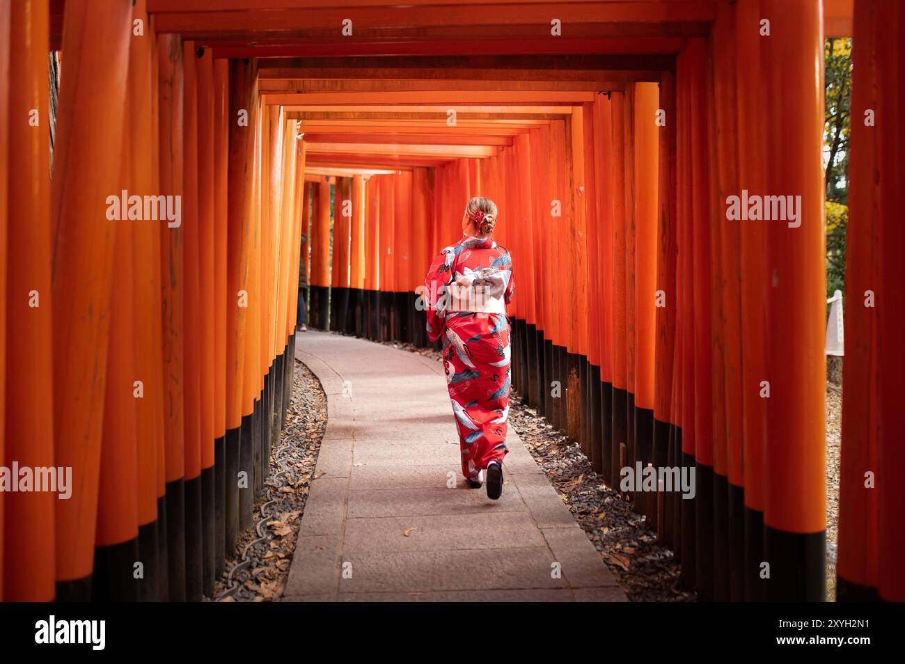 A woman dressed in a traditional red kimono walks through a tunnel of ...