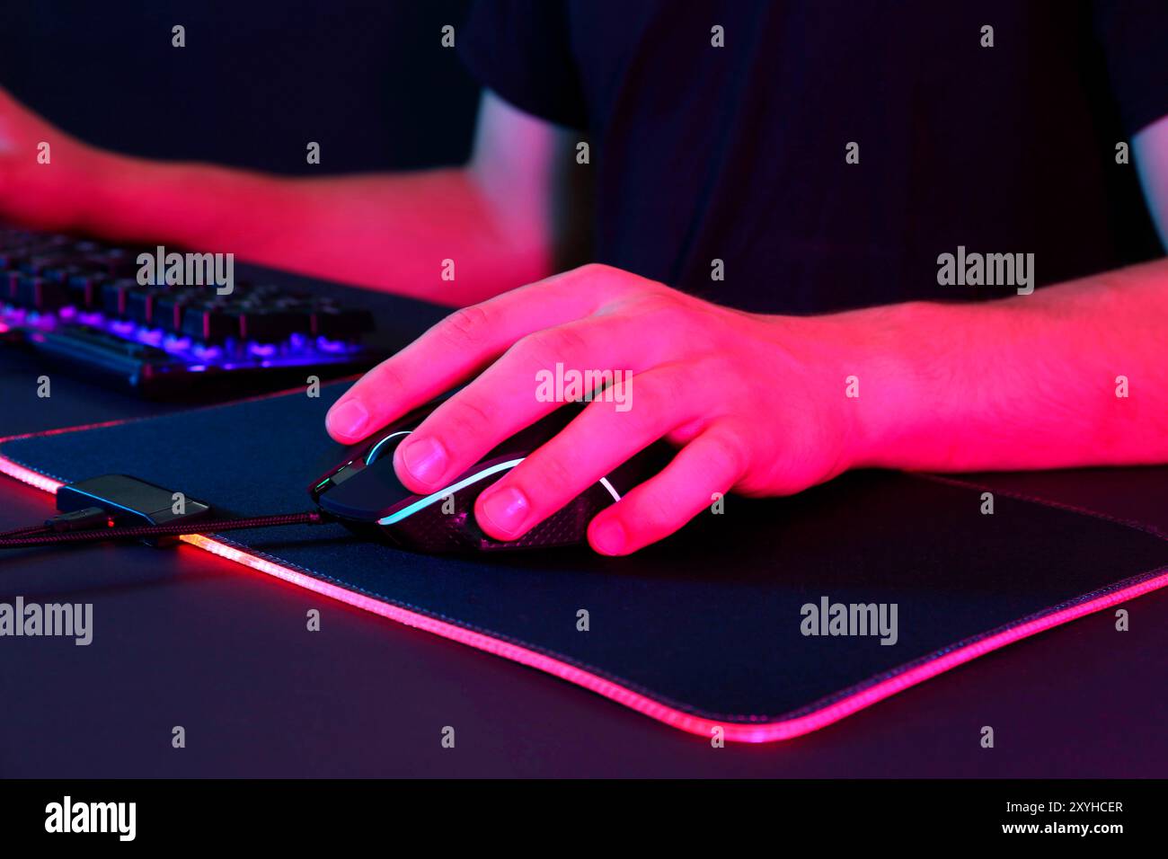 Gamer using modern wired computer mouse in neon lights at black table ...