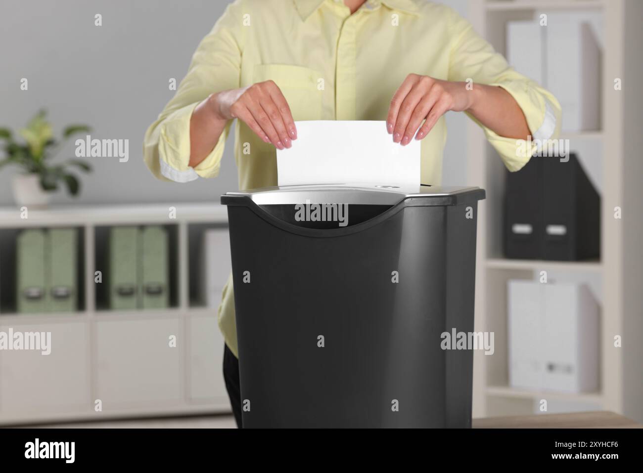 Woman destroying sheet of paper with shredder in office, closeup Stock Photo