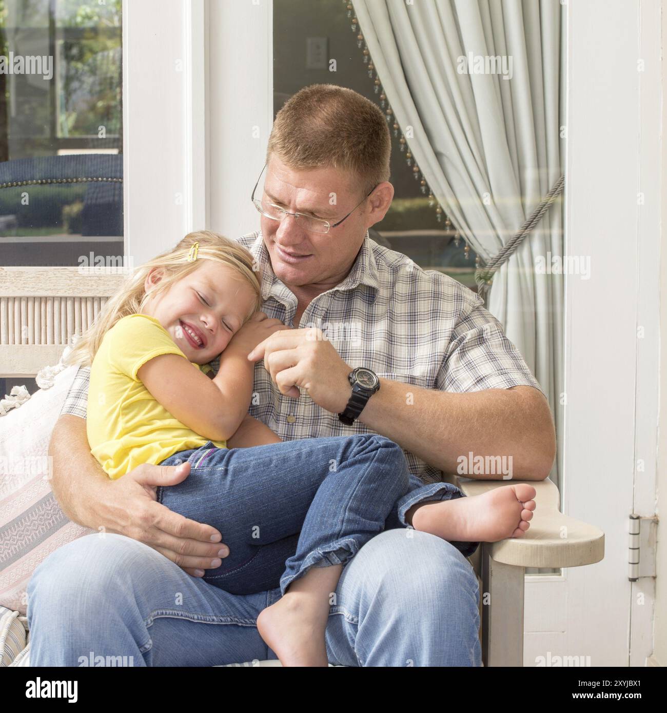 A father and his daughter spend quality time together as they sit on the patio with the father on the bench and his young daughter in his lap Stock Photo