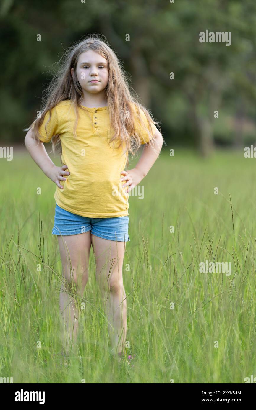 Young girl standing with hands on hips in tall grass field Stock Photo ...
