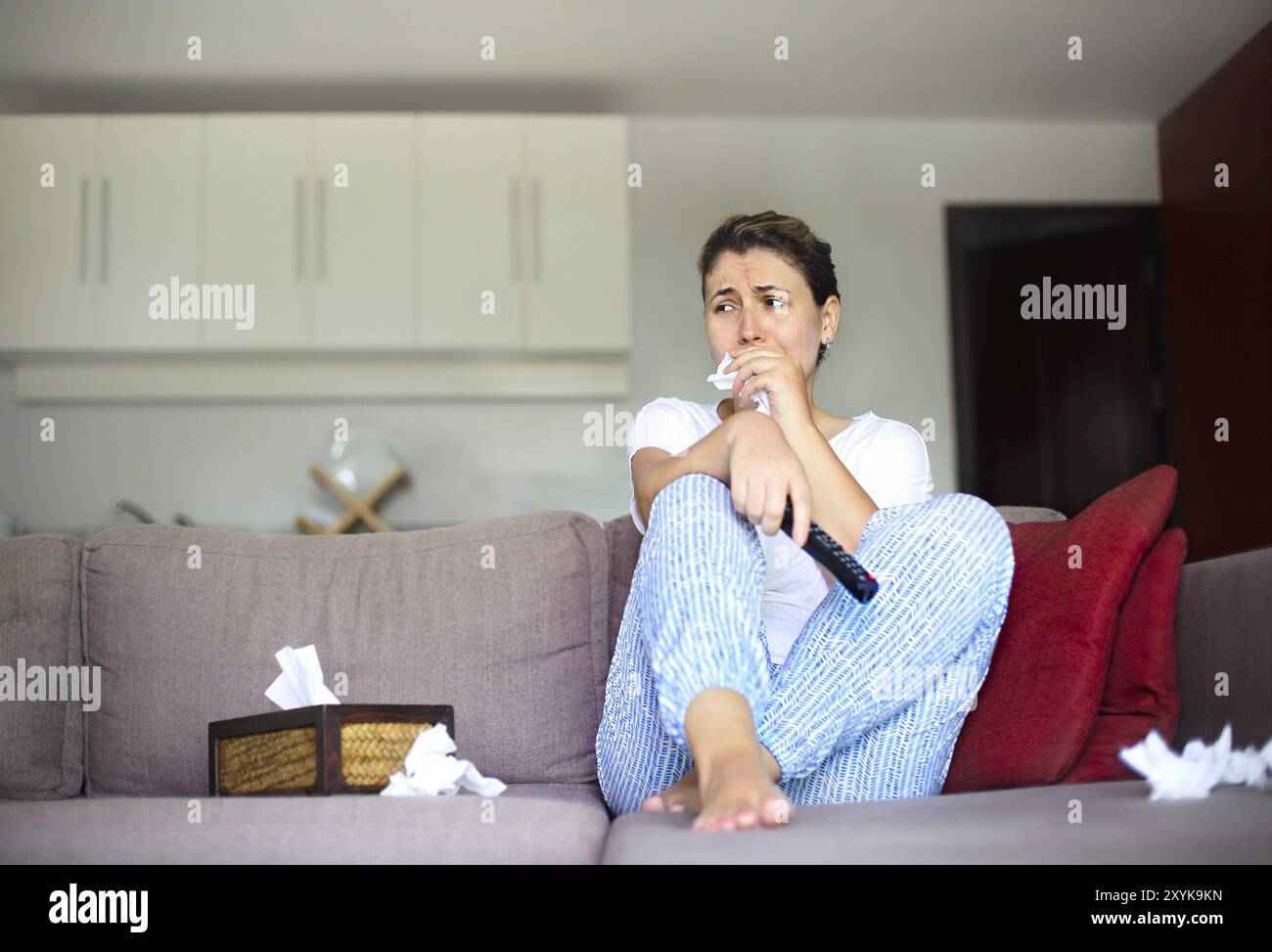 Portrait of young sad woman sitting on sofa and watching tv at home ...