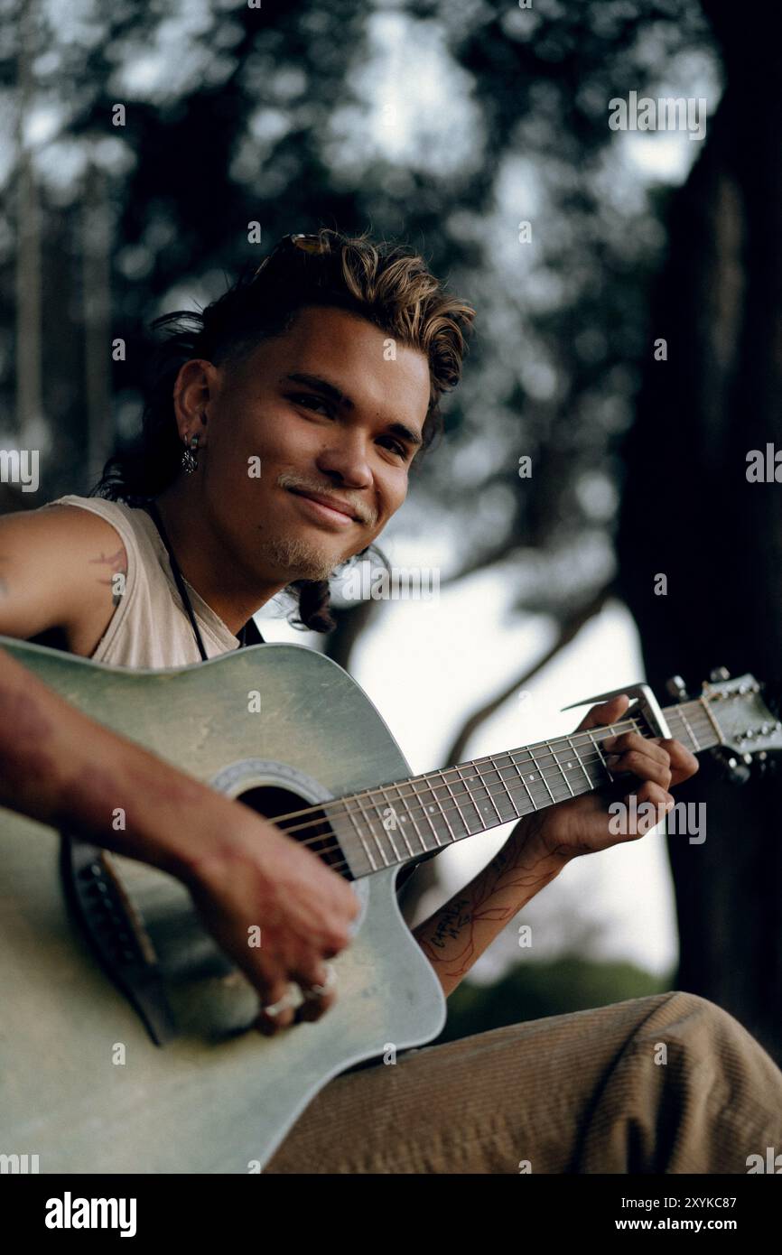 A young man plays a guitar in the park at sunset. Stock Photo