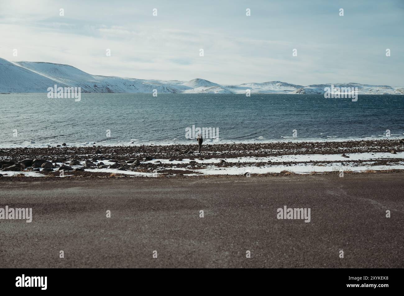 Man standing at an Icelandic lake, surrounded by snowy mountains Stock Photo