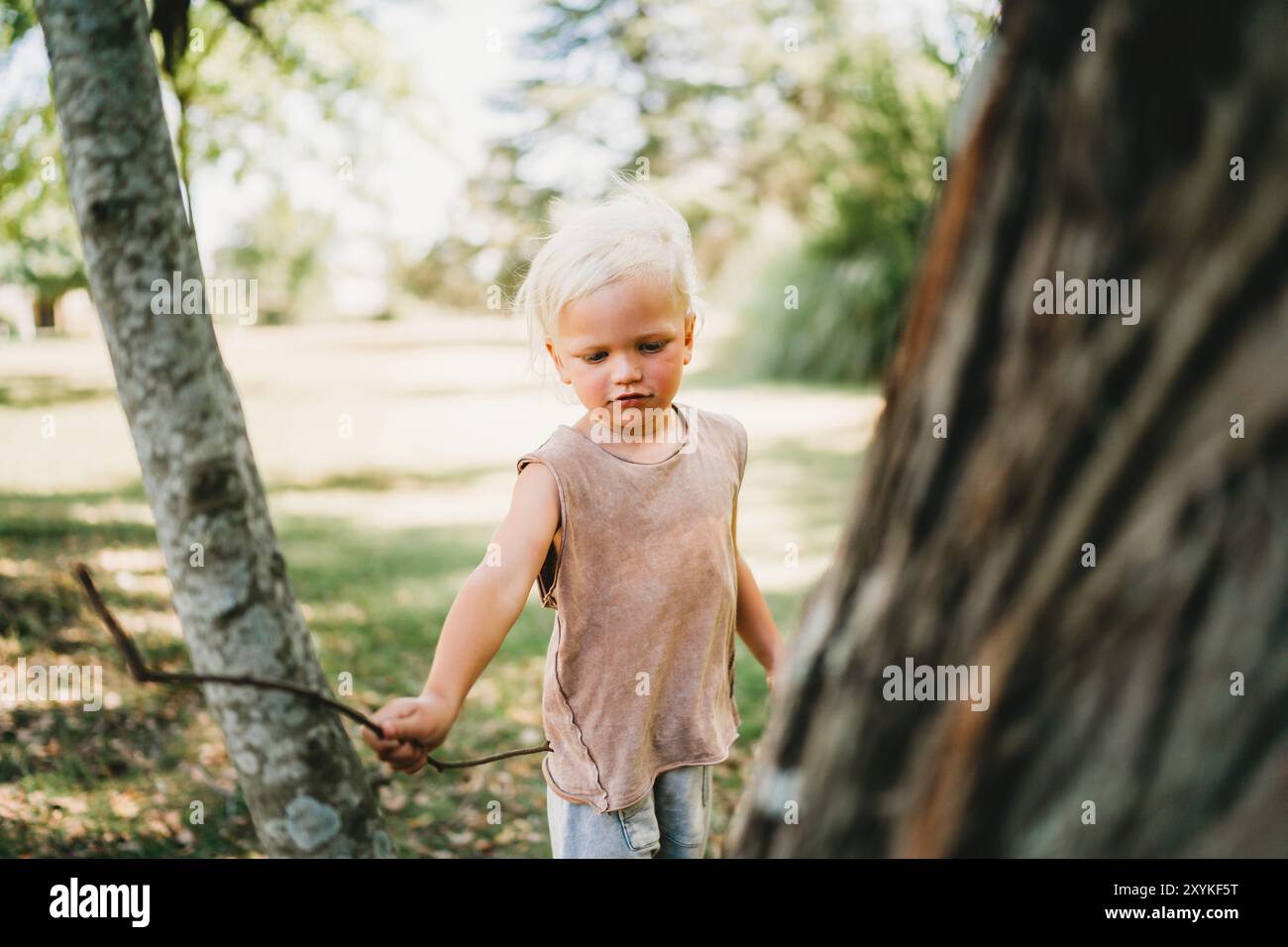 Adorable blonde child playing with stick at park on summer day Stock Photo