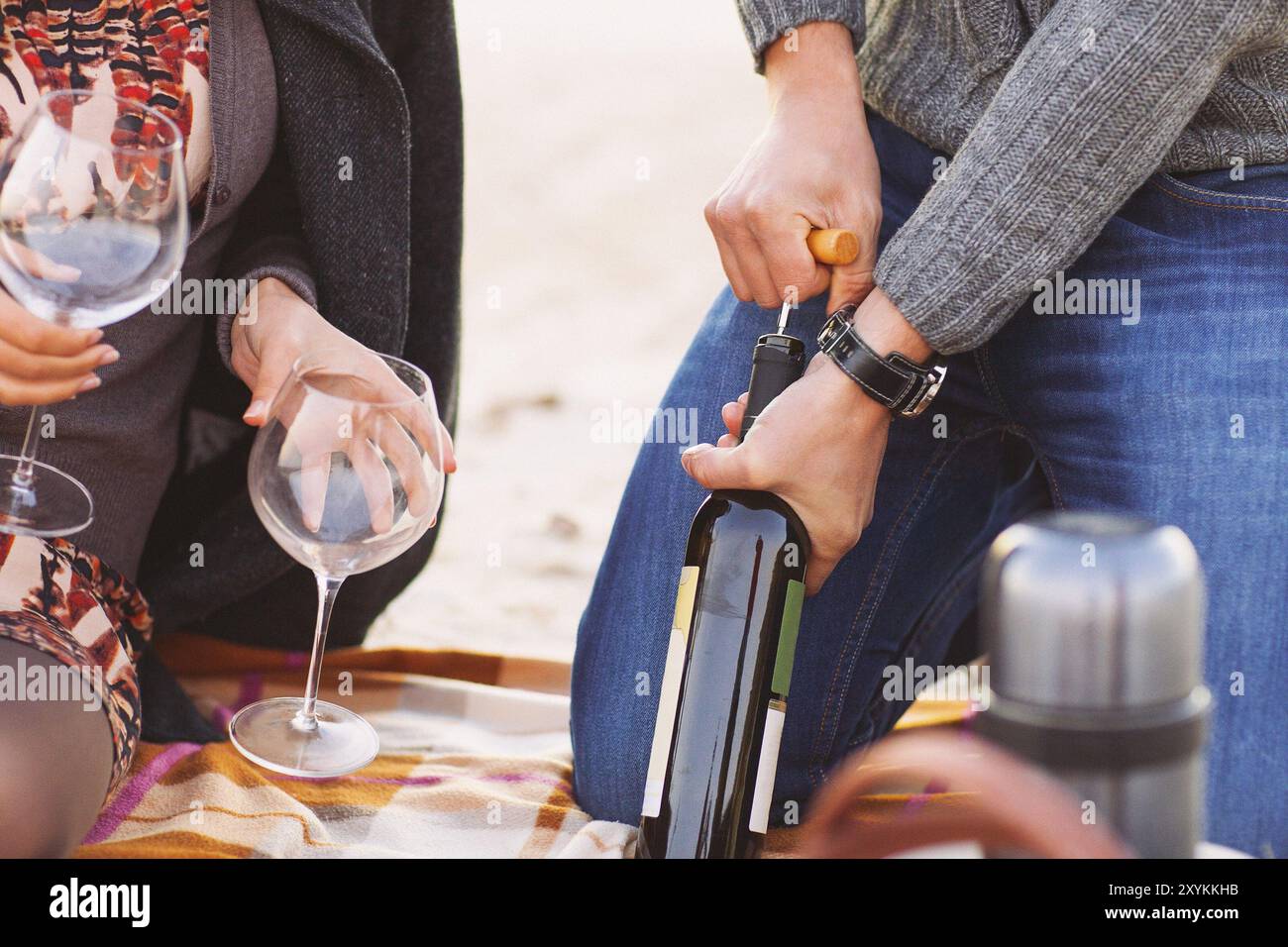 Young happy couple enjoying picnic on the beach together. Man opening bottle of wine. Close up Stock Photo
