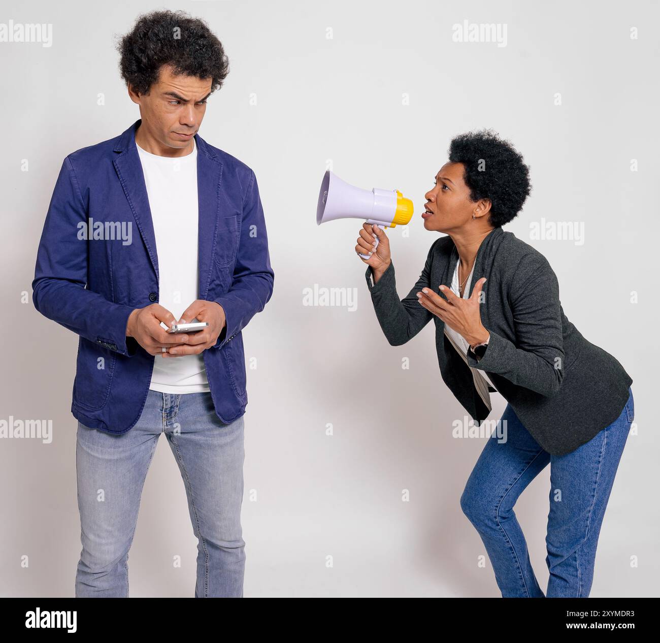 Angry businesswoman with megaphone yelling at male coworker using mobile phone on white background Stock Photo