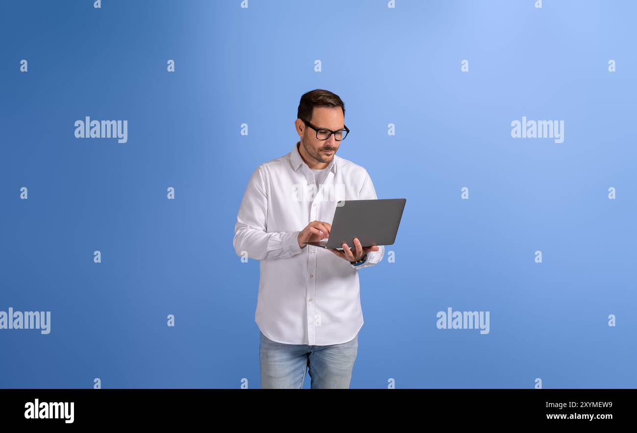 Serious handsome businessman checking e-mails over wireless computer and standing on blue background Stock Photo