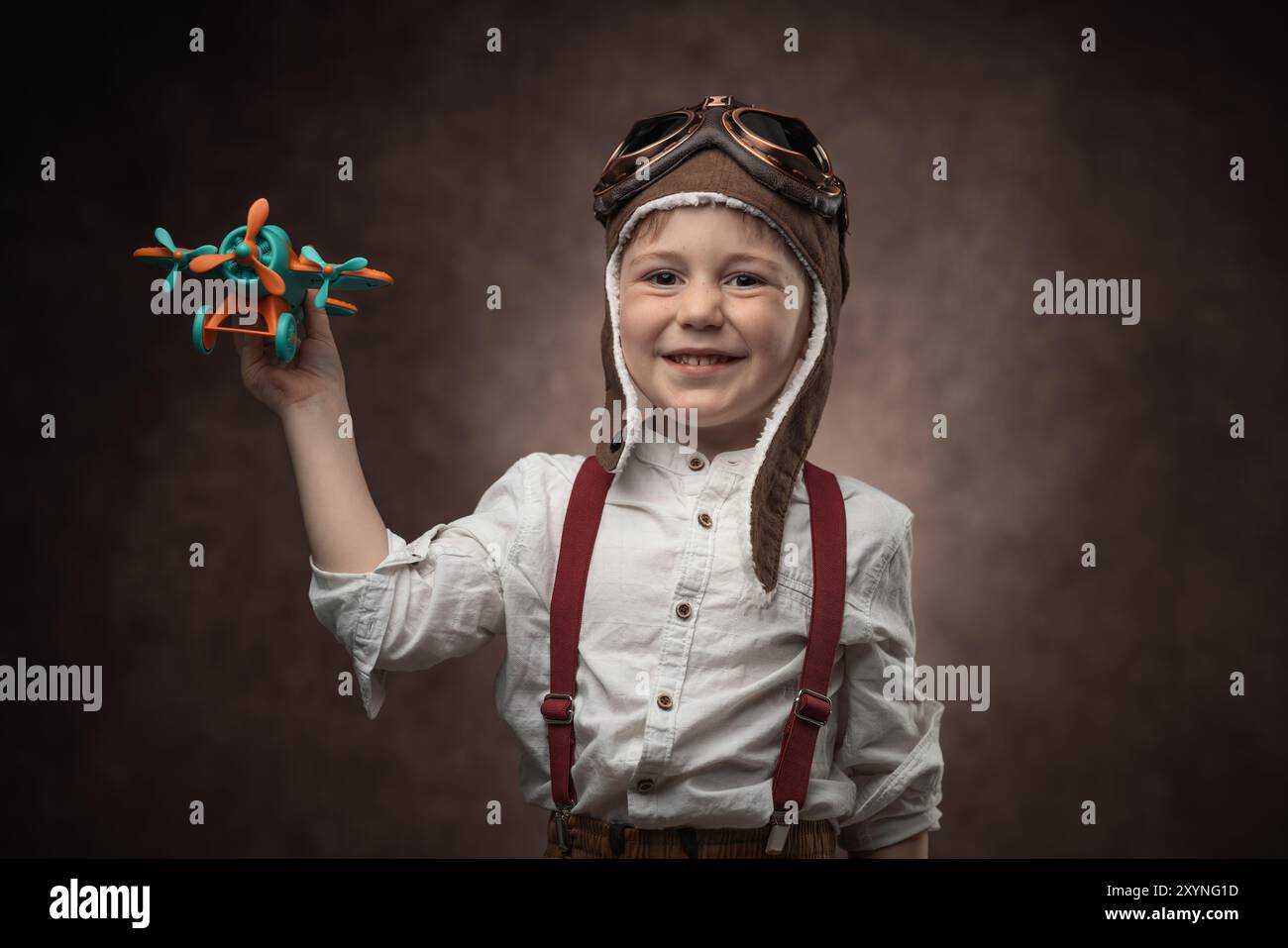 Child pilot with aviator cap and toy airplane, retro portrait of a boy ...