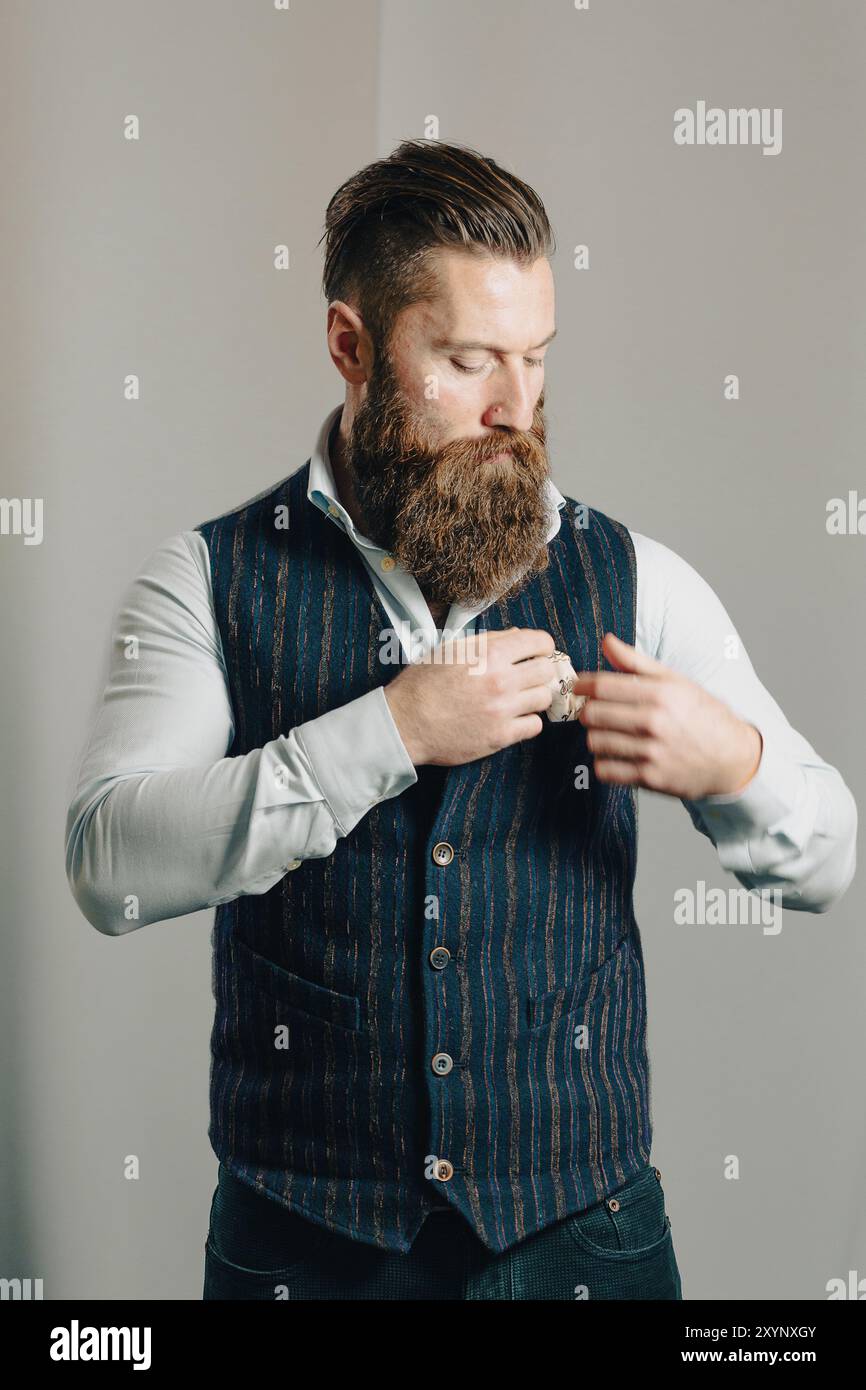 Casually dressed businessman with a beard is buttoning his waistcoat while getting ready for work Stock Photo