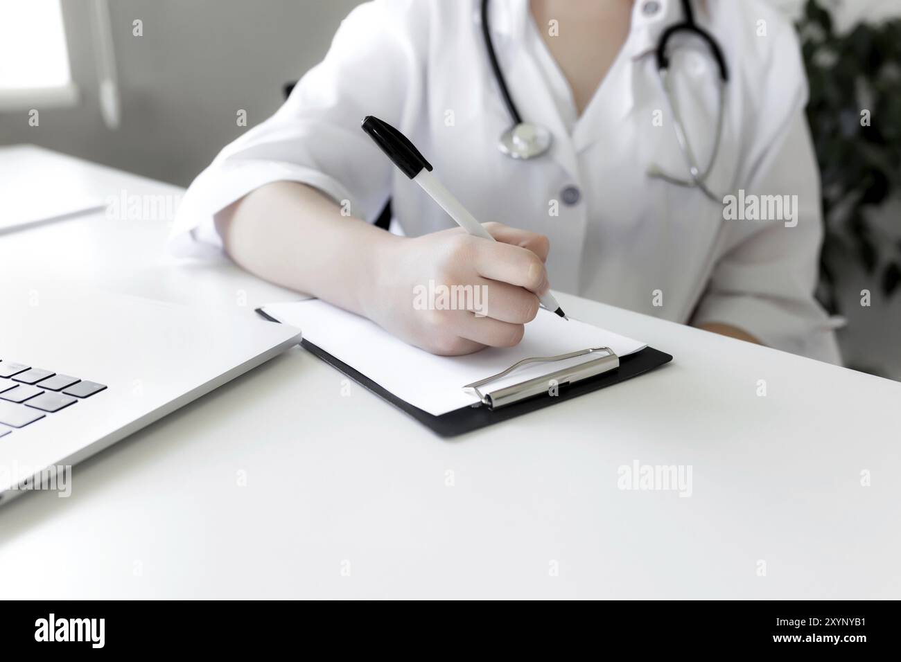 The doctor in white uniform dress with stethoscope writes something in the patient's medical history, consulting patient and doing medical exam. Stock Photo